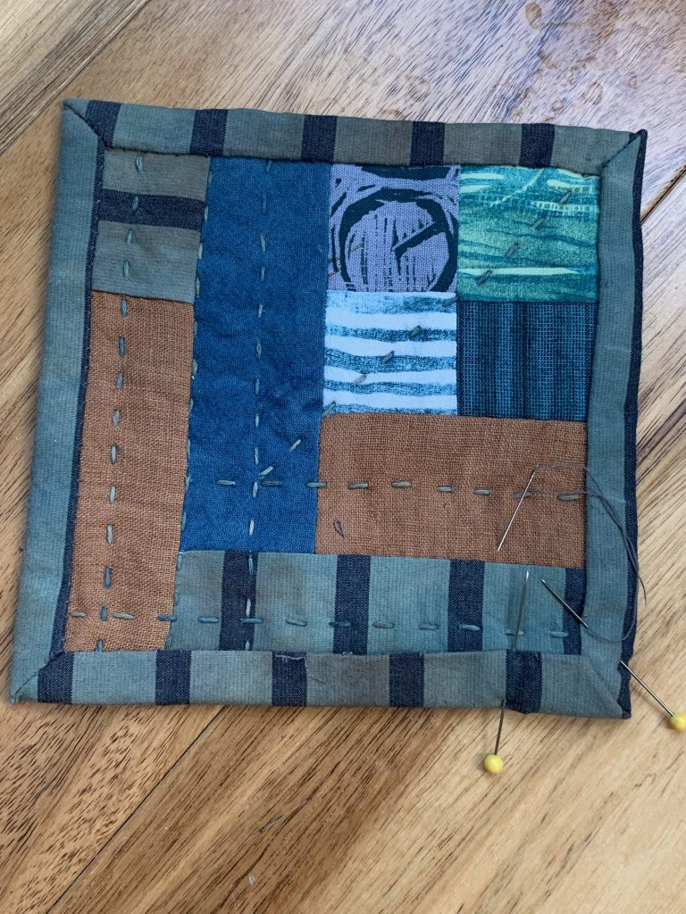 A tiny handmade quilt in blue and brown fabrics.